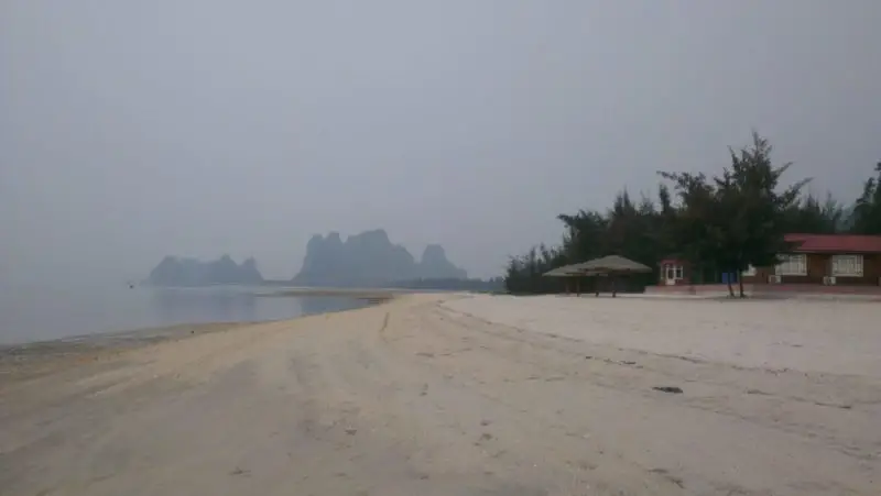 A sabdy beach with karst peaks in the background at Van Don Peninsular, north of Halong Bay
