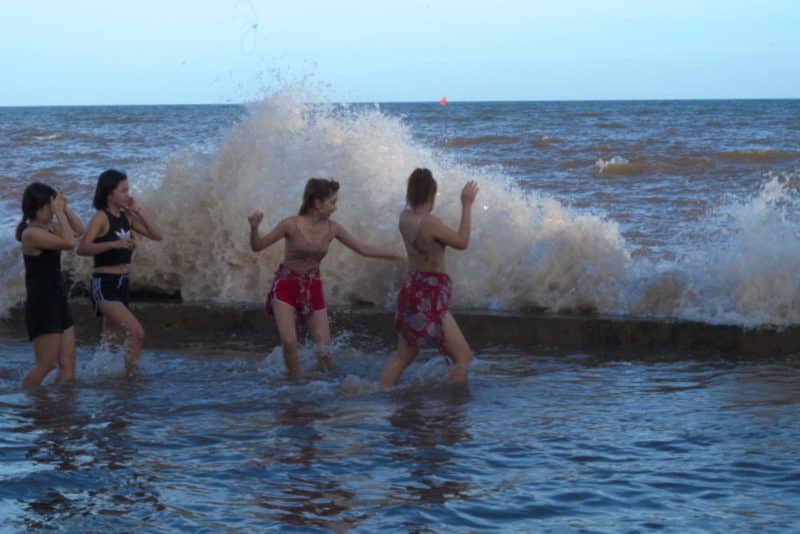 Waves crashing into girls swimming at king tide on the coast of Nam Dinh in Vietnam