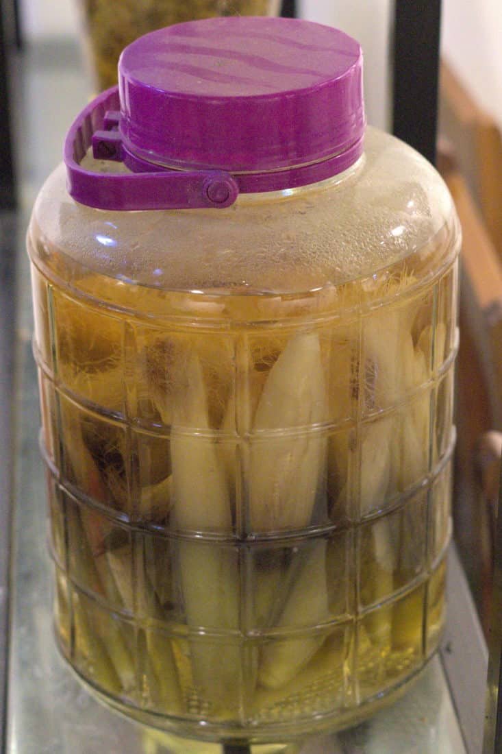 Green corn soaking in a large glass jar of rice wine