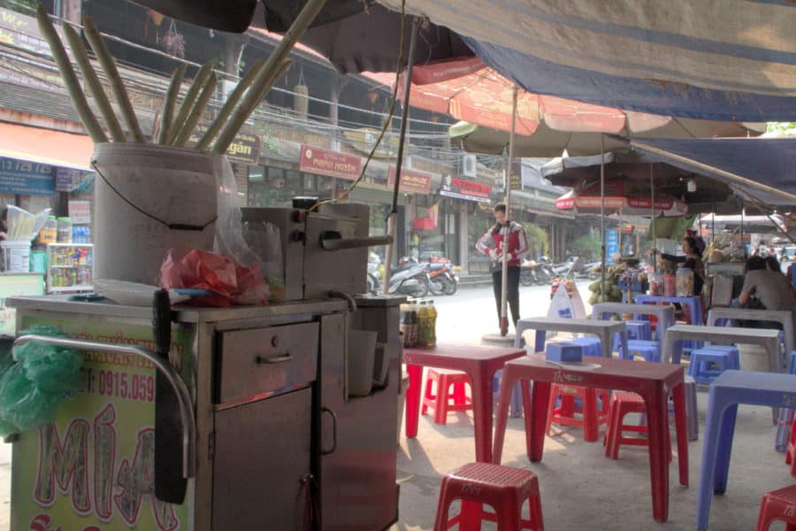 A nuoc mia stall with small plastic chairs and tables next to a ceramics market