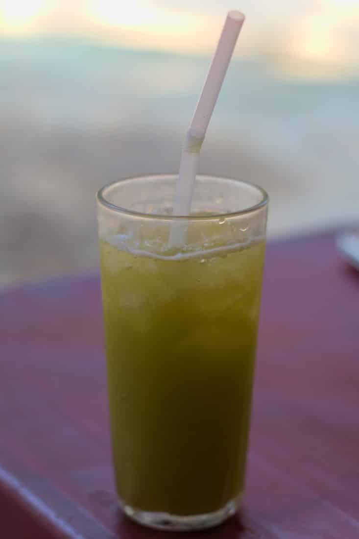 Fresh sugarcane juice with ice and a straw sitting on a plastic table