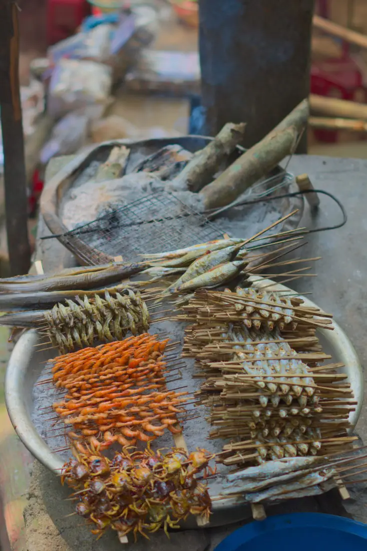 Skewers of lake  fish, crabs, and shrimp being barbecued on a metal bowl of hot coals