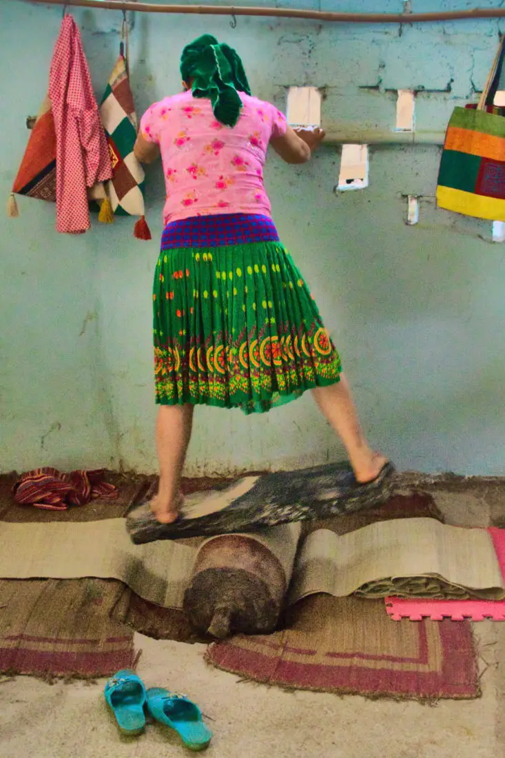 A woman standing on a plank and log rolling side to side  in order to soften fabric underneath