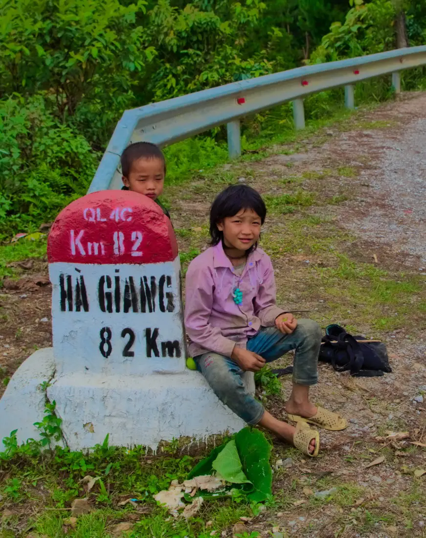 Two Vietnamese boys sitting next to a Ha Giang road marker on a motorbike tour