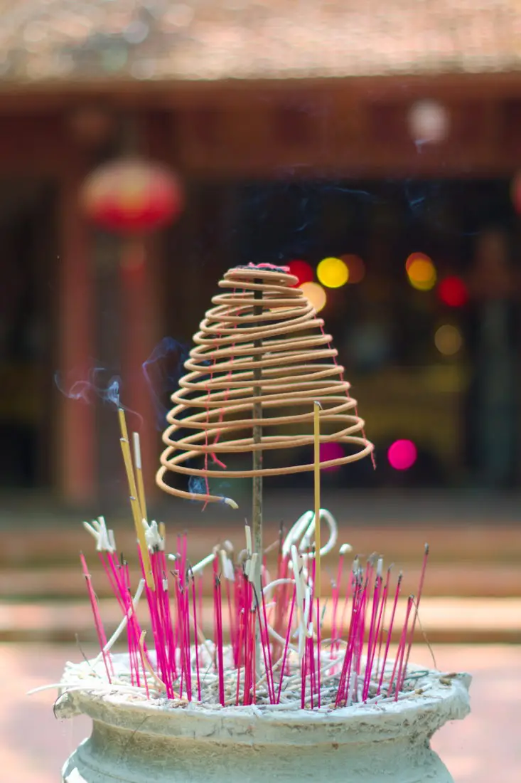 Sticks and a spiral of incense burning in front of  a traditional temple asan offering