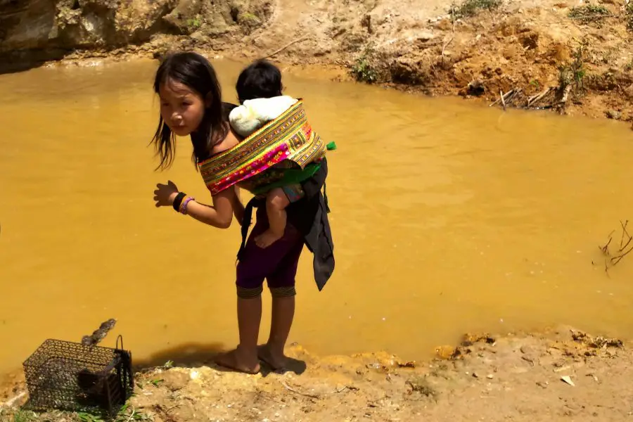 Mong girl child a baby on her back next to water
