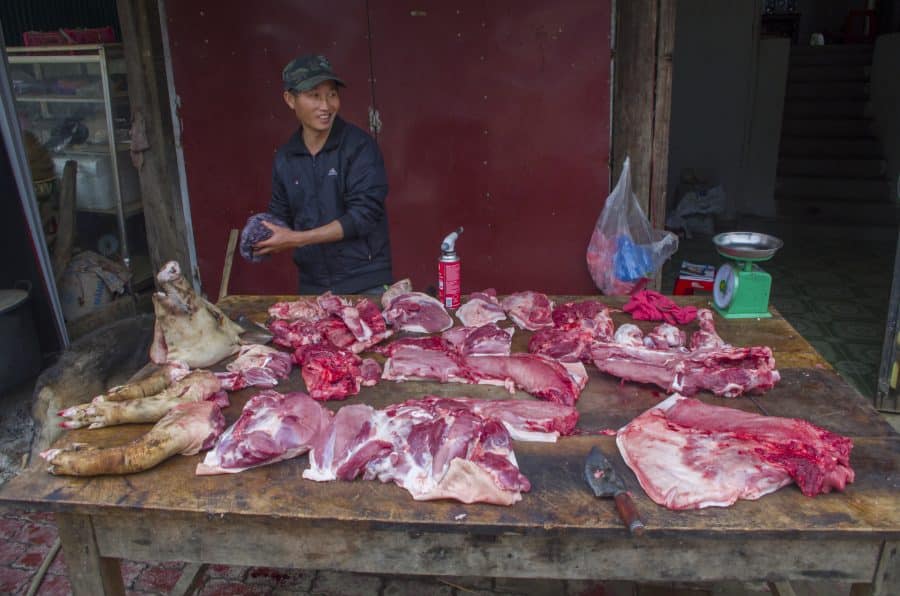 A vietnamese butcher behind a table of cut pork