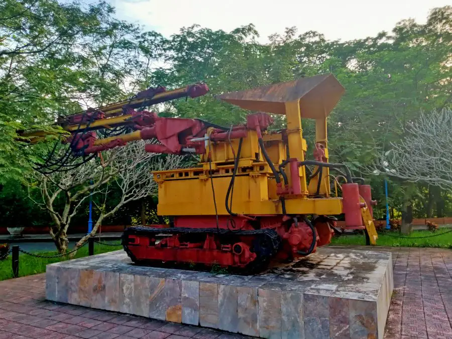 An old red and yellow drilling rig on display in a park